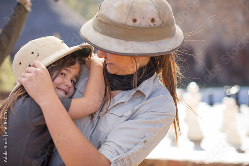Happy girl embracing young woman wearing pith helmet photo