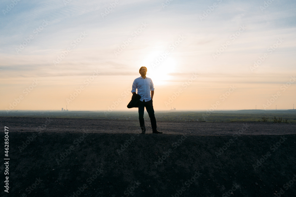 Male entrepreneur standing on hill against sky during sunset Male entrepreneur standing on hill against sky during sunset