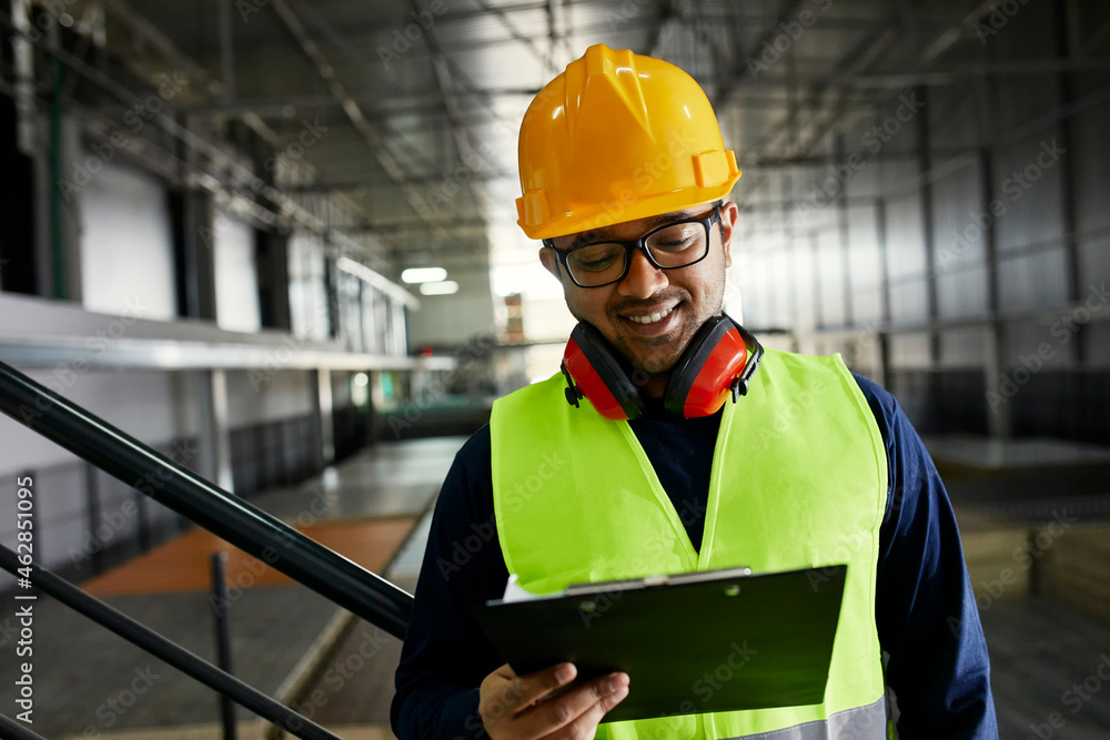 Smiling worker holding clipboard in factory warehouse Smiling worker holding clipboard in factory warehouse