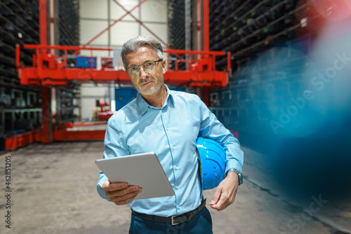 Mature businessman holding tablet in a high rack warehouse of a factory photo