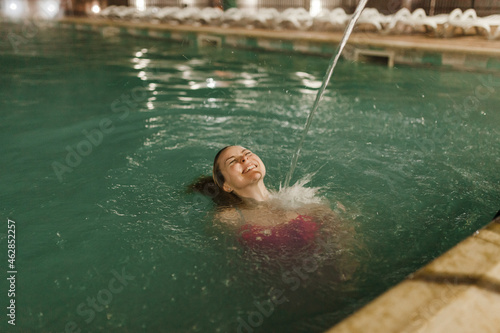 Water splashing on cheerful woman swimming in thermal pool at night photo