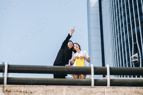 Smiling businesswoman pointing female coworker at downtown district in city against clear sky photo