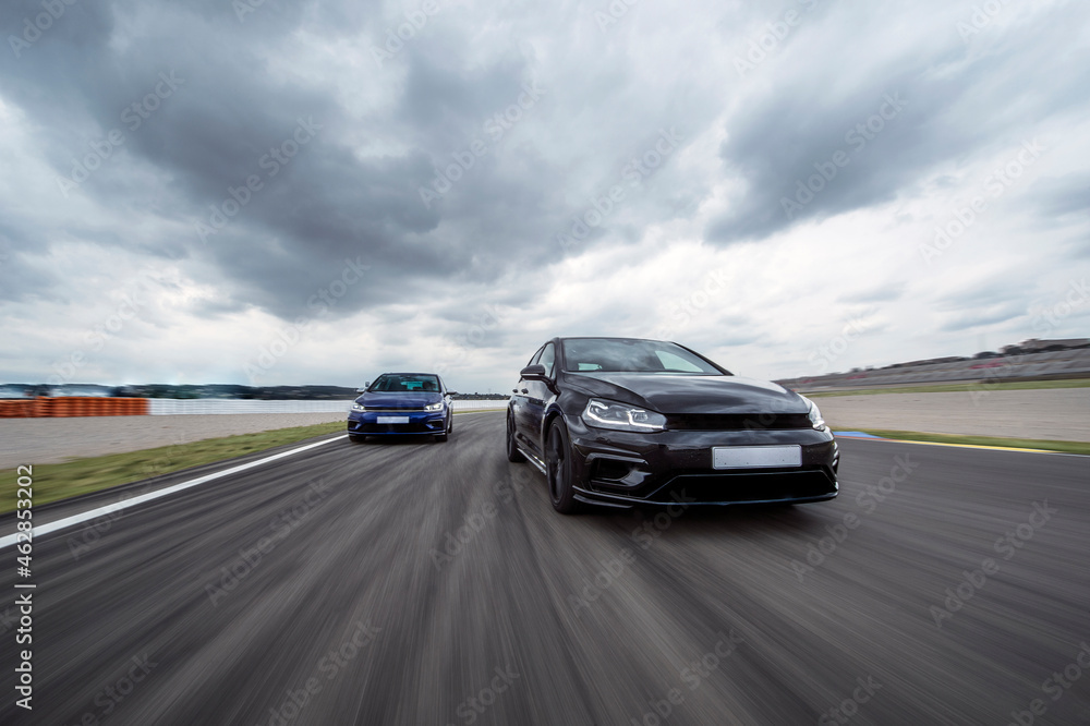 Cloudy sky over two sports cars racing on asphalt track Cloudy sky over two sports cars racing on asphalt track