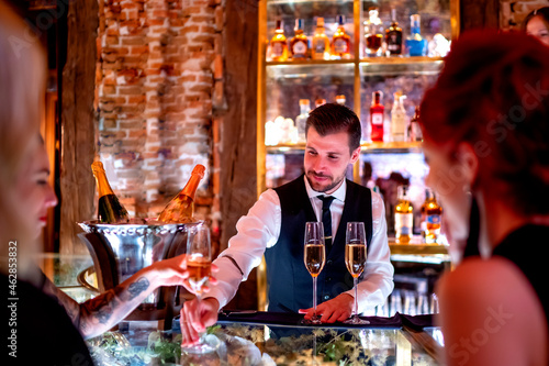 Bartender serving drink to women at bar counter in pub photo