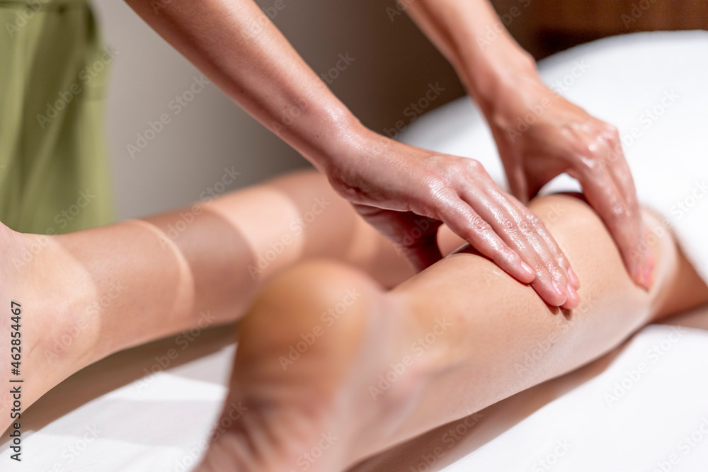 Mature female therapist massaging woman's leg at table in health spa Mature female therapist massaging woman's leg at table in health spa