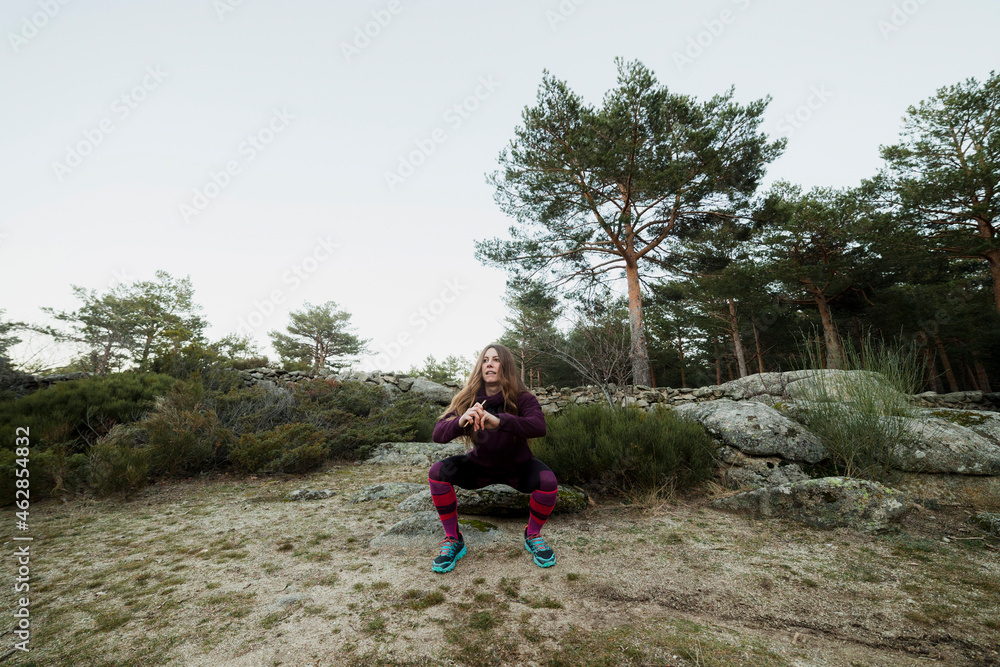 Mid adult woman doing squatting exercise in forest Mid adult woman doing squatting exercise in forest