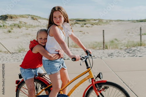 Younger sister embracing girl while sitting on bicycle during sunny day photo