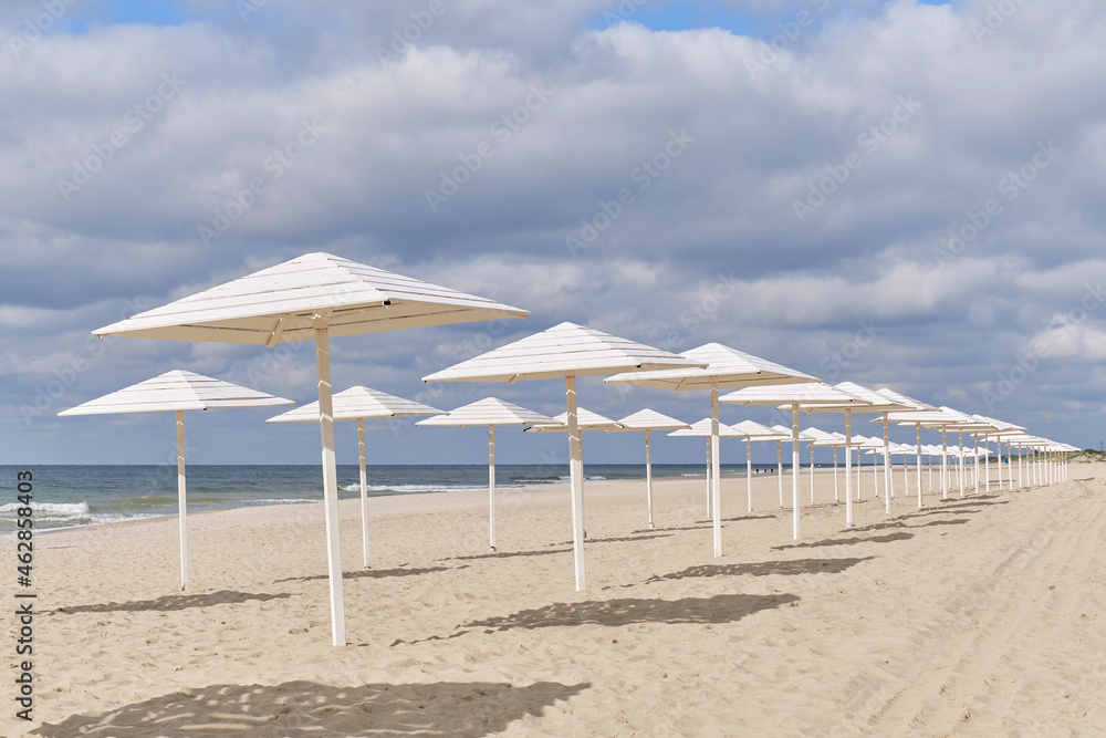 Baltic deserted sandy beach with white wooden sun umbrellas in autumn. Seaside landscape