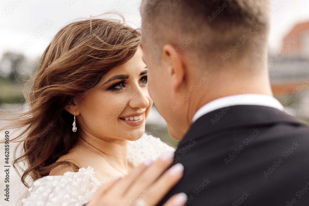 portrait of bride, beautiful and gentle, looks lovingly at her groom, who is standing with his back to camera. happy moments - wedding day. portrait of bride, beautiful and gentle, looks lovingly at her groom, who is standing with his back to camera. happy moments - wedding day.