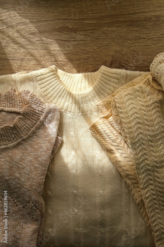 White and beige sweaters on wooden background, illuminated by sunlight. Flat lay.