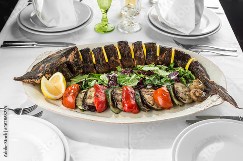grilled Whole sturgeon Fish with lemon and grilled vegetables on plate