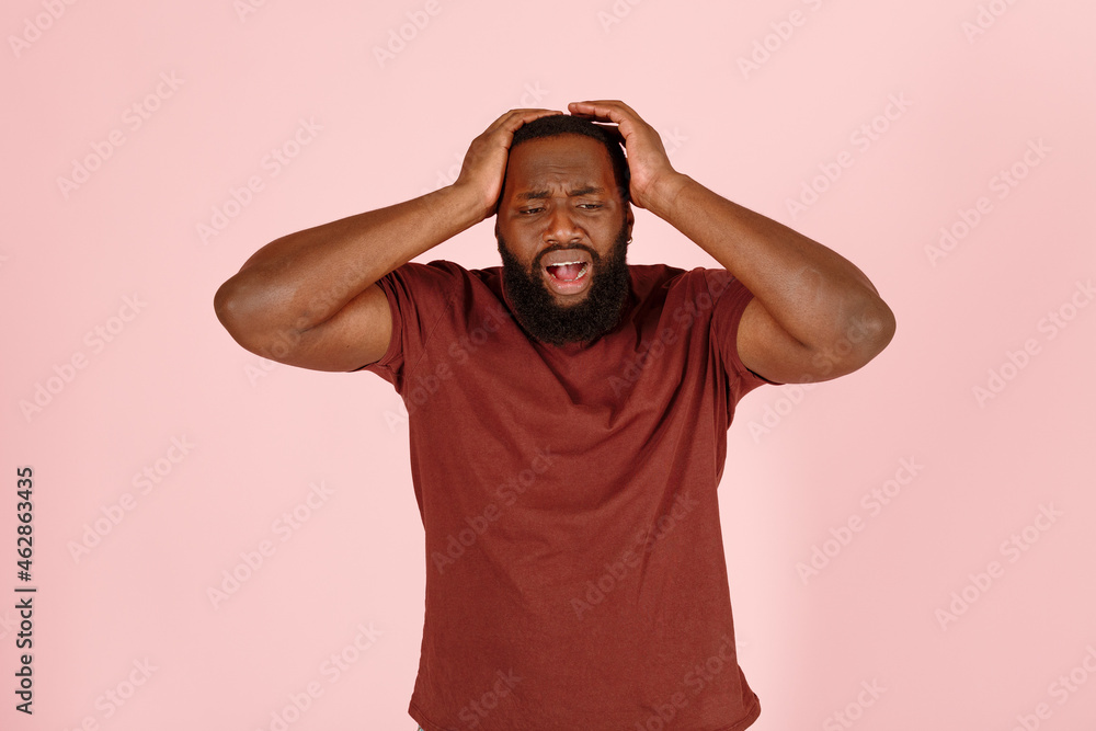 Bearded African-American man patient in t-shirt suffers from severe headache standing on pink background in studio closeup Bearded African-American man patient in t-shirt suffers from severe headache standing on pink background in studio closeup