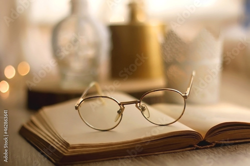 Open book, reading glasses, various candles and vase with flowers. Hygge at home. Selective focus.