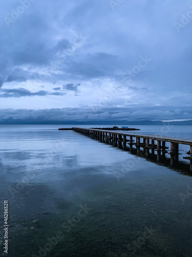 Long pier at the lake, twilight, dark blue and gray sky and lake, mountains background