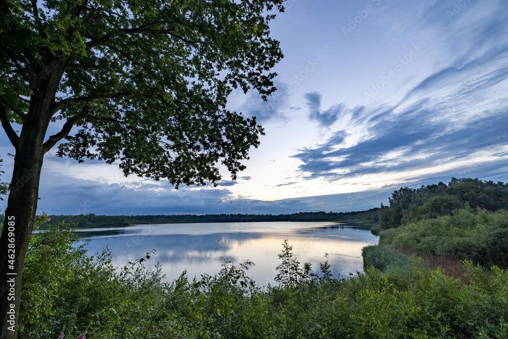 a beautiful blue lake with green tree in the foreground under a dramatic blue dusk sky. High quality photo