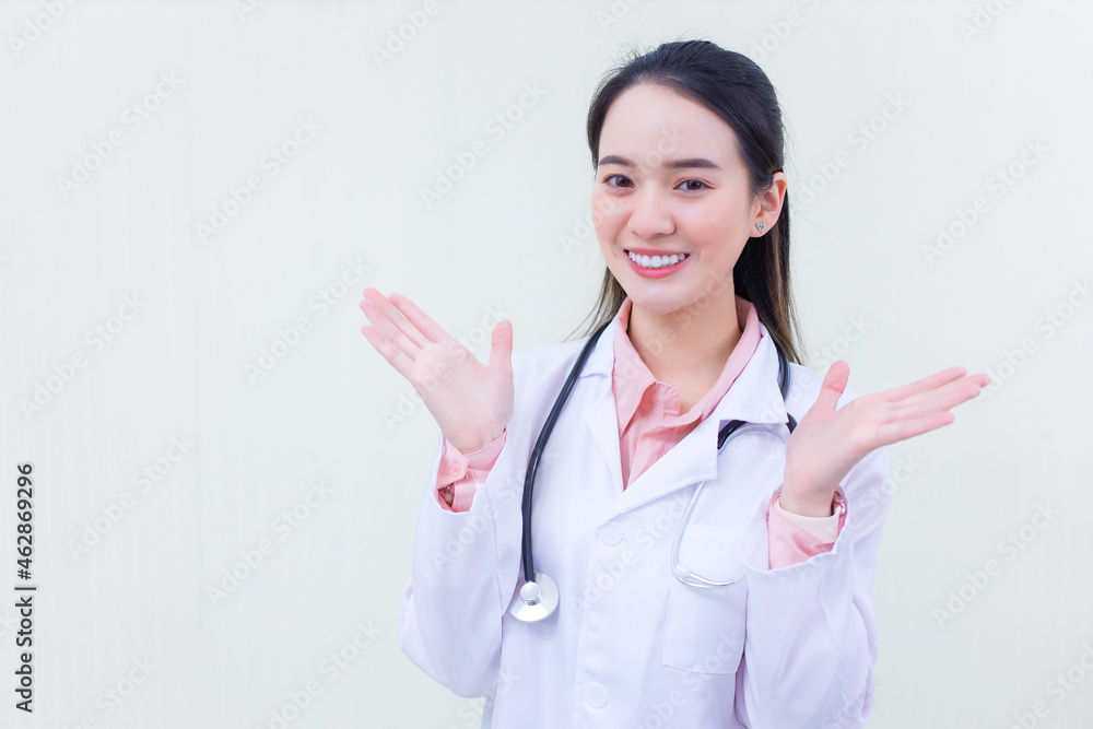 Beautiful young Asian woman smiling cheerfully gestures in a white doctor's gown against a white background. Beautiful young Asian woman smiling cheerfully gestures in a white doctor's gown against a white background.