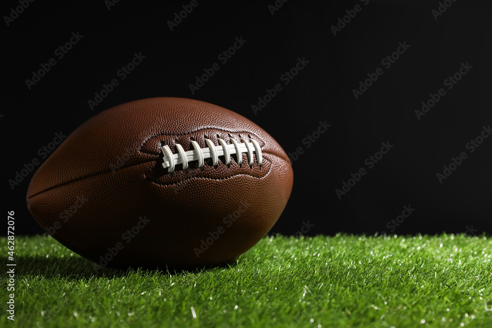 Obraz premium American football ball on green grass against black background. Space for text