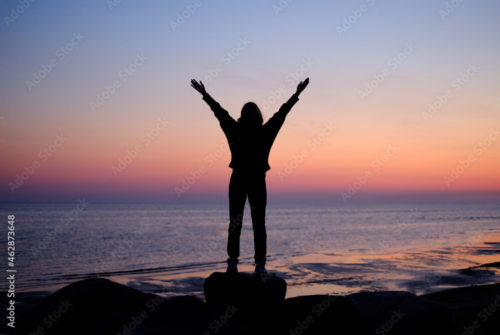 Silhouette of woman with raised hands on the beach at sunset