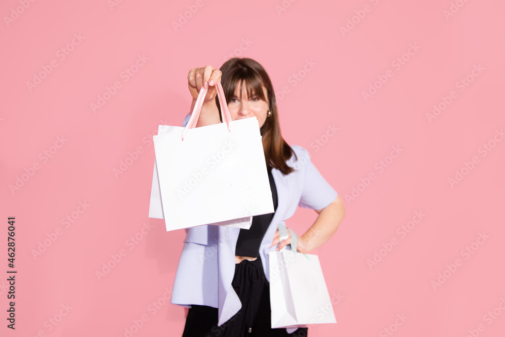 photo of lovely young woman in casual clothing is happy with gift bags, shopping for spring holiday on pink background in studio. Celebrating Woman's Day, birthday, Valentine's, anniversary.