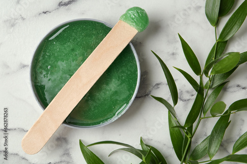 Spatula with wax and leaves on white marble table, flat lay photo