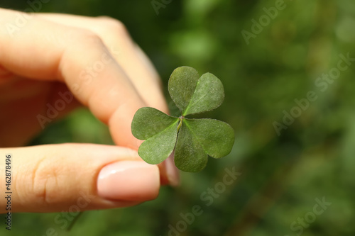 Woman holding green clover leaf outdoors, closeup