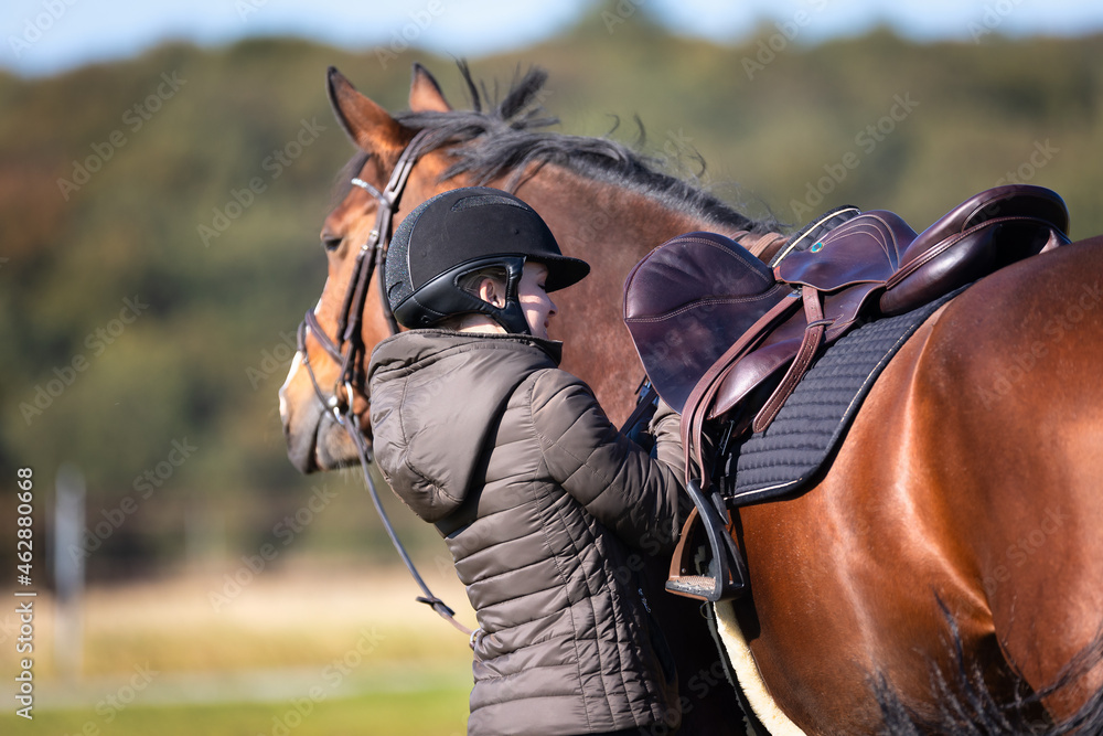 Obraz premium Rider re-girding her saddle, recorded from the direction of the horse's hindquarters..