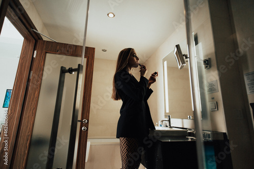 a young beautiful girl in the bathroom, she is wearing a black jacket on a naked body and high boots, the sunlight from the window brightly illuminates her