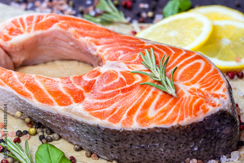 Raw red salmon fish slices with spices, rosemary and lemon in the kitchen on light background. Raw red salmon fish slices with spices, rosemary and lemon in the kitchen on light background.