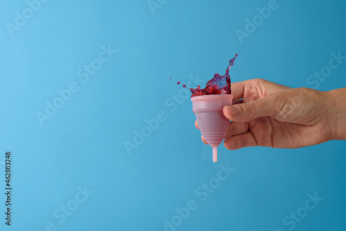 Blood splash in menstrual cup. Hand holding it on blue background photo