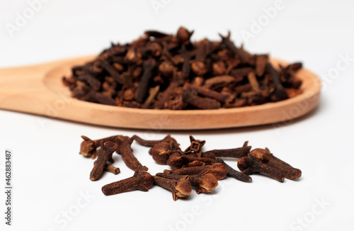 dried cloves in a wooden spoon, on a white background. spicy herb for food flavor and natural medicine