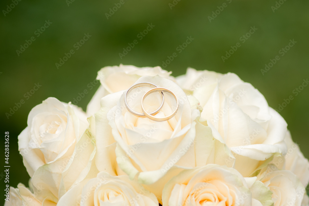 White rose wedding bouquet with two golden wedding rings, romance or valentines day concept with copy space. Close-up view and green background. White rose wedding bouquet with two golden wedding rings, romance or valentines day concept with copy space. Close-up view and green background.