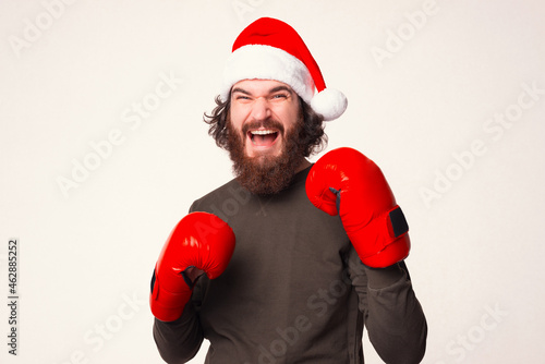 Bearded screaming man is standing in ready to attack position, while wearing Christmas hat and boxing gloves.