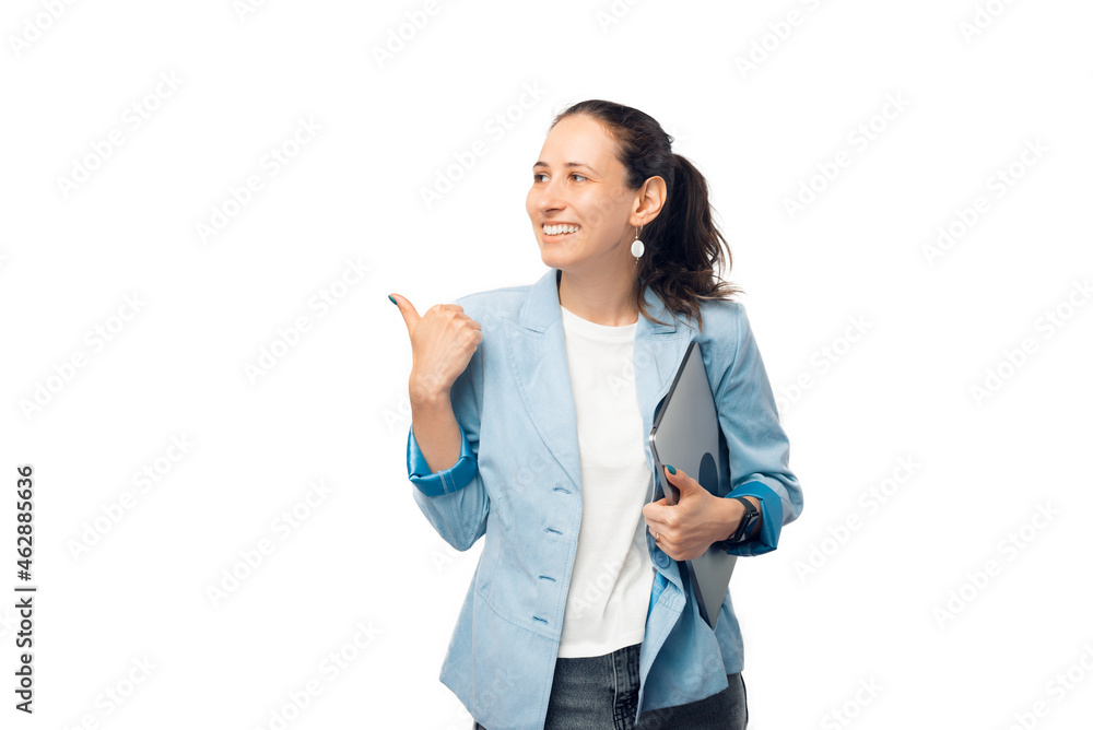 Positive woman, holding a closed laptop is pointing with her thumb aside. Positive woman, holding a closed laptop is pointing with her thumb aside.