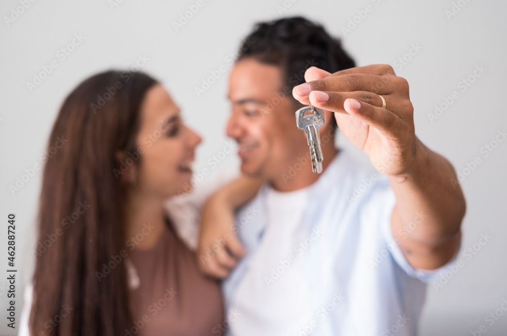 Close up of home keys showed from happy young interracial couple in background - concept of new house purchase and bank loan economy business - real estate and people owners Close up of home keys showed from happy young interracial couple in background - concept of new house purchase and bank loan economy business - real estate and people owners