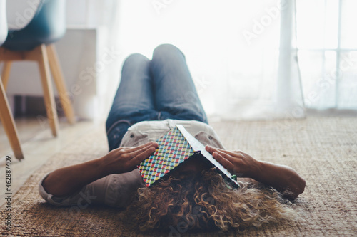 Woman lay down on the floor on carpet sleeping because tired with book to cover eyes. Female people asleep during the day in living room. Insomnia disease health concept photo