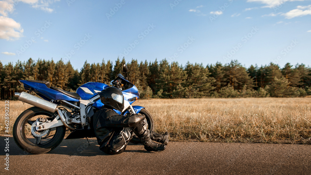 Fototapeta premium Motorcycle driver in helmet and leather jacket sits on the asphalt road next to a sports motorcycle