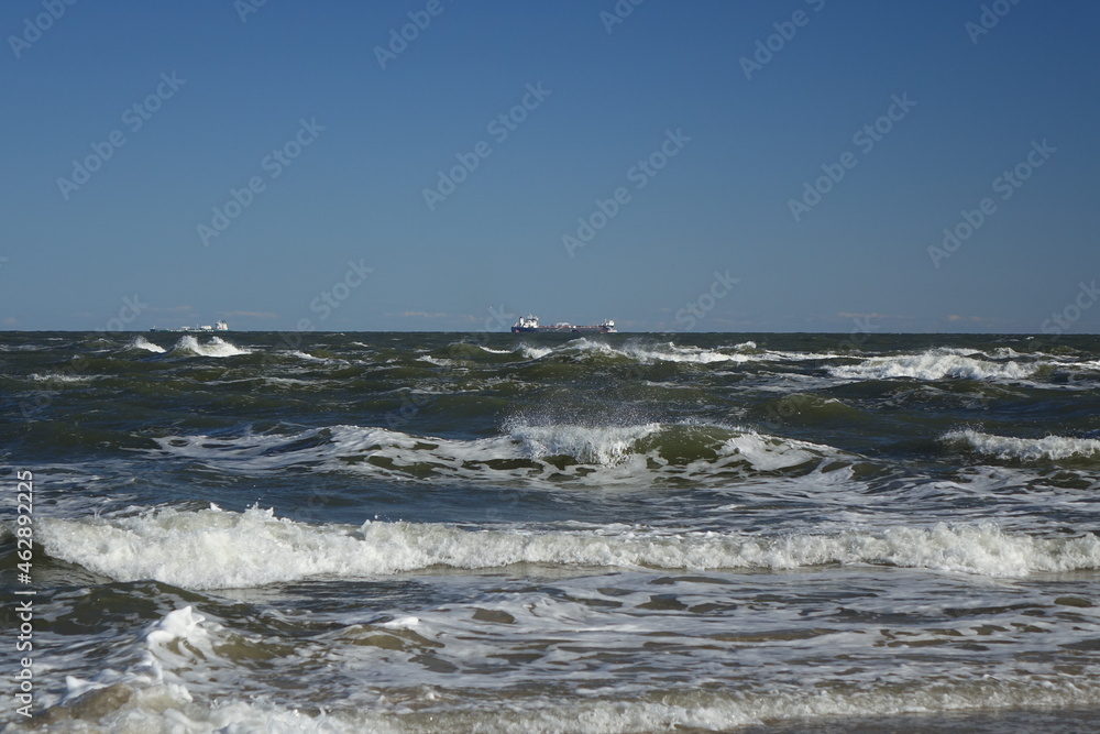 Rough waters at Skagen Nordstrand with cargo ship in the background near Cape Grenen, meeting point of Skagerrak and Kattegat and the northernmost point of Denmark, Skagen, Northern Jutland, Denmark

