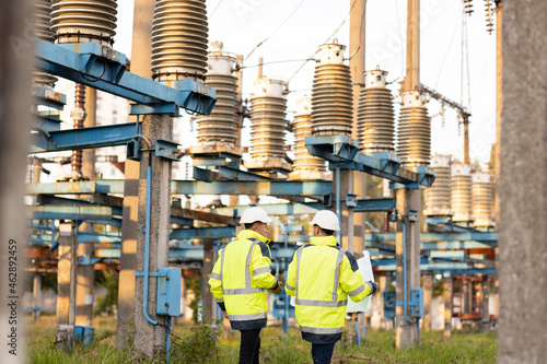 Engineers men in warm clothes use digital tablet computer discuss work walking against power electric substation