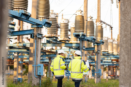 Engineers men in warm clothes use digital tablet computer discuss work walking against power electric substation photo