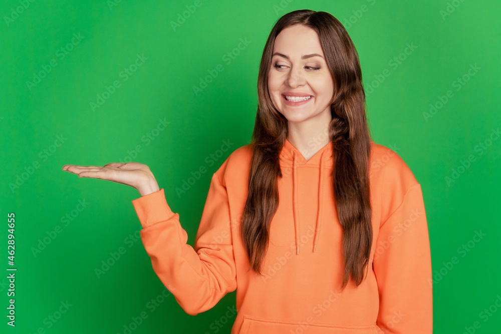 Portrait of curious teen charming lady open palm hold blank space look product on green background Portrait of curious teen charming lady open palm hold blank space look product on green background