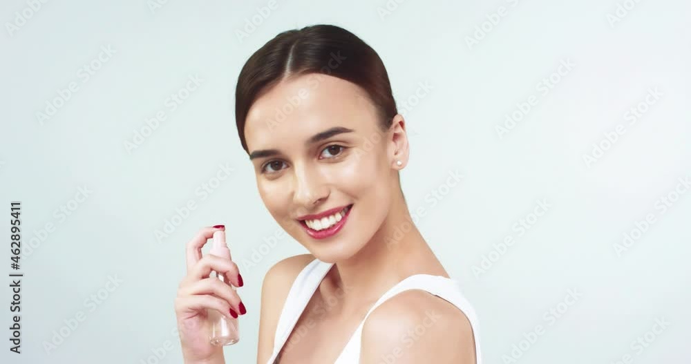 Beautiful caucasian woman with gathered hair applies moisturizing spray on her face and looking at camera smiling. Beautiful caucasian woman with gathered hair applies moisturizing spray on her face and looking at camera smiling.