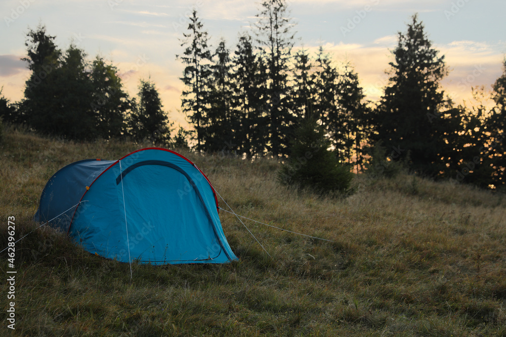 Blue camping tent on hill near forest, space for text