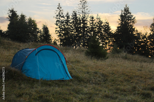Blue camping tent on hill near forest, space for text