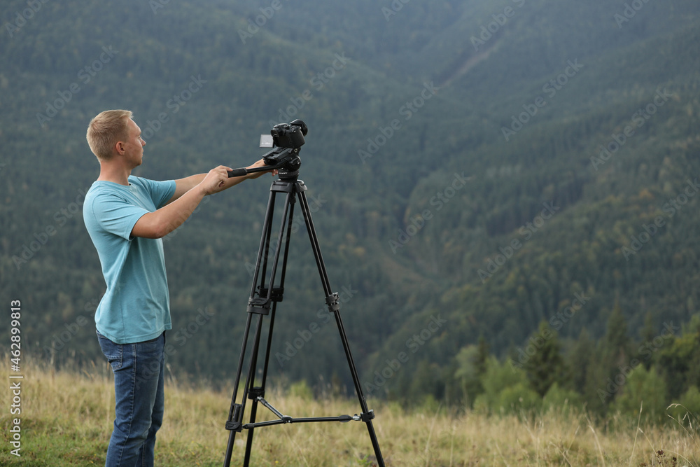 Photographer taking video with modern camera on tripod in mountains