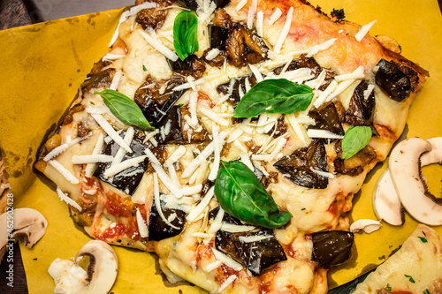 top view of a mouth watering Big squared pizza slice with eggplant, basil leaves, mushrooms and cheese on a plate ready to be served photo