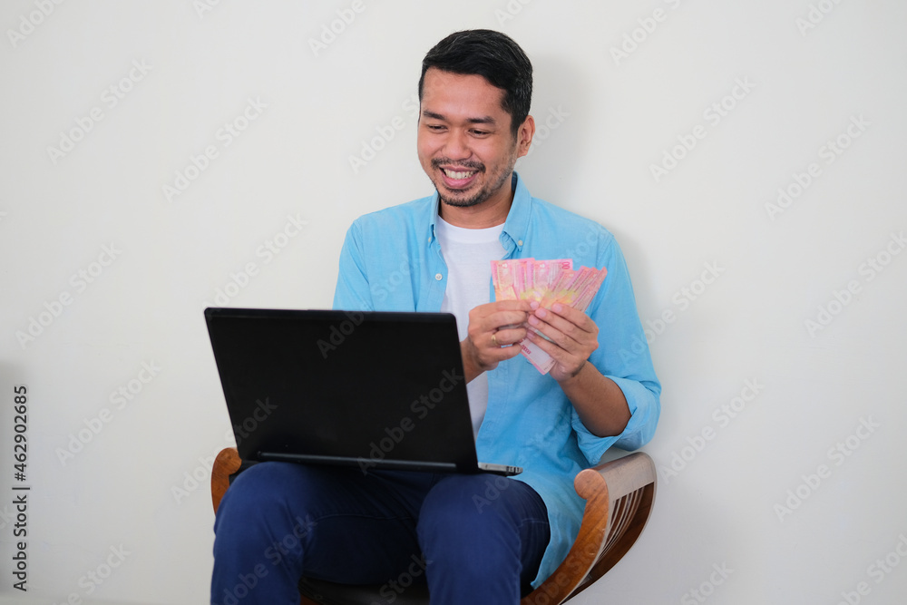 Adult Asian man showing happy expressin while counting money that he earn Adult Asian man showing happy expressin while counting money that he earn
