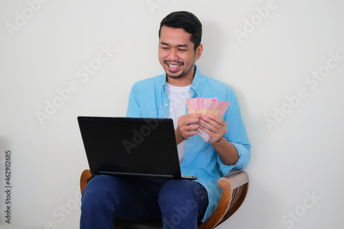 Adult Asian man showing happy expressin while counting money that he earn photo