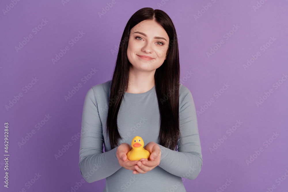 Photo of young attractive girl holding yellow bath duck toy playful isolated over purple color background Photo of young attractive girl holding yellow bath duck toy playful isolated over purple color background