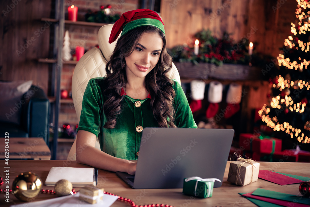 Photo of young woman serious santa helper elf sit desk work latop assistant xmas indoors inside house home Photo of young woman serious santa helper elf sit desk work latop assistant xmas indoors inside house home