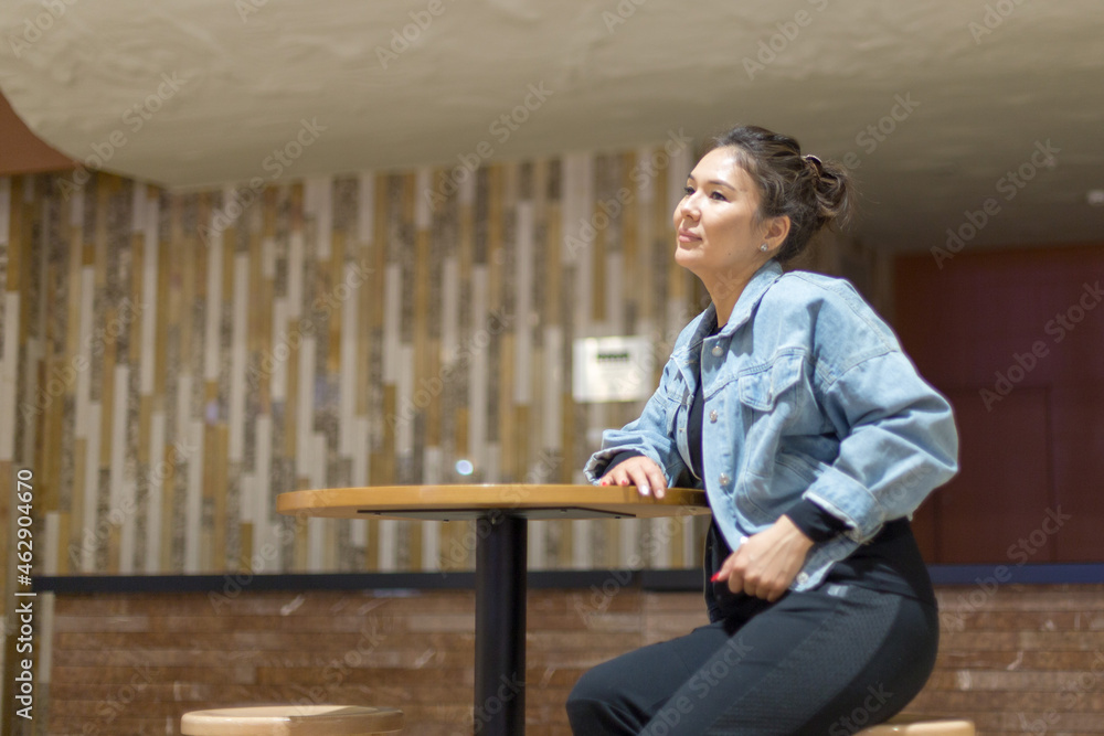 girl in blue denim clothes sitting on a high bar stool in a cafe and posing for the camera, relaxed mood girl in blue denim clothes sitting on a high bar stool in a cafe and posing for the camera, relaxed mood